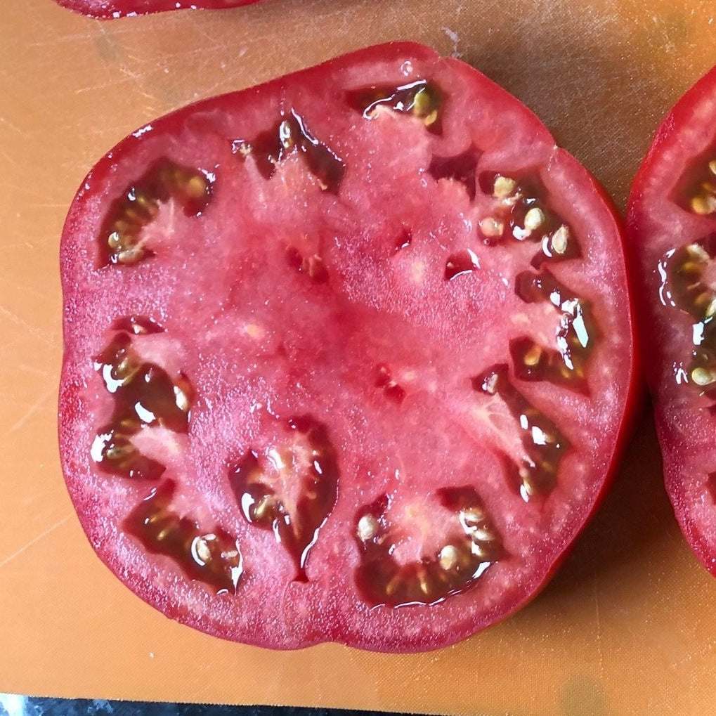 Beefsteak heirloom tomato sliced in half, showing juicy, meaty interior.