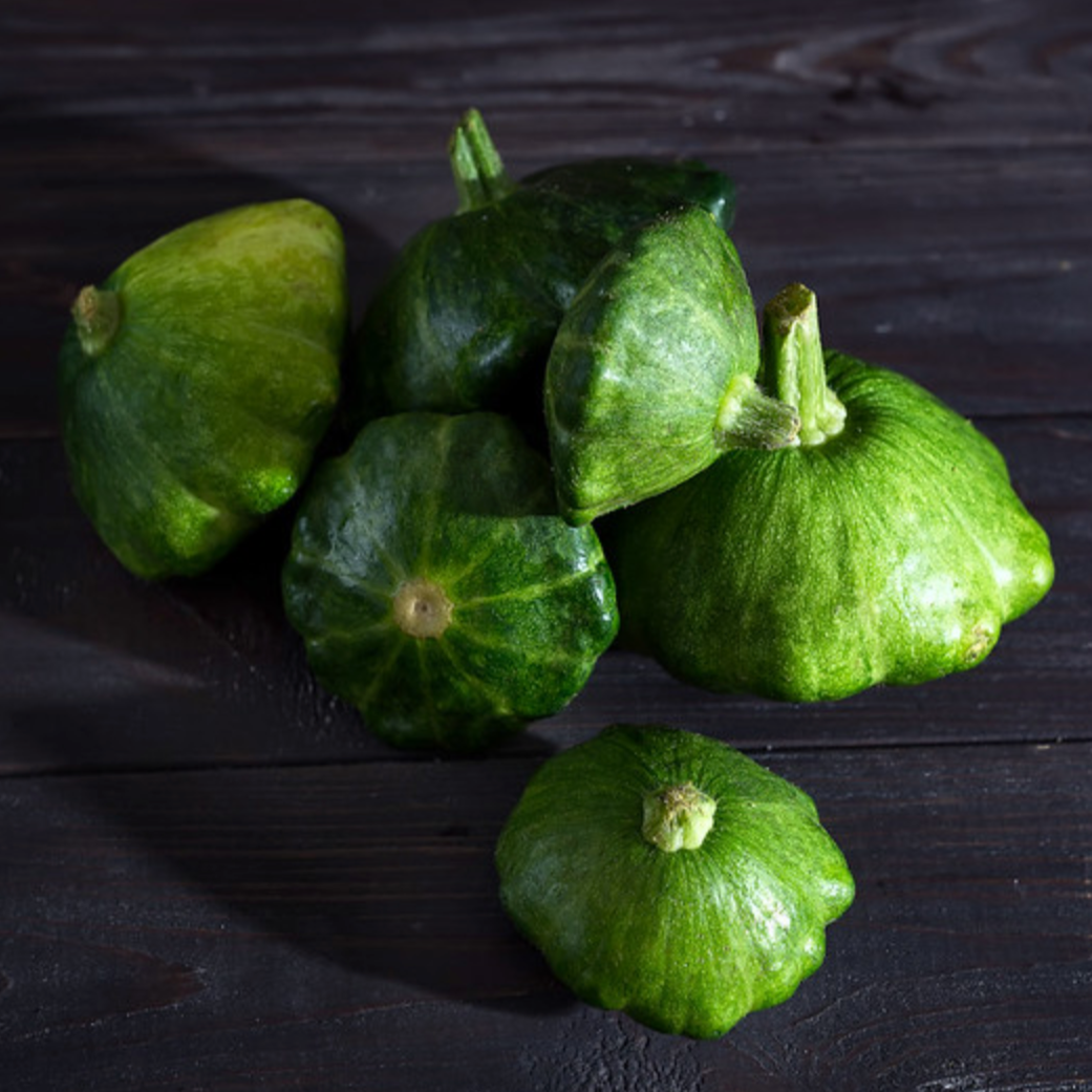 Squash Total Eclipse F1 with deep green and white speckled fruits on a dark wooden surface.