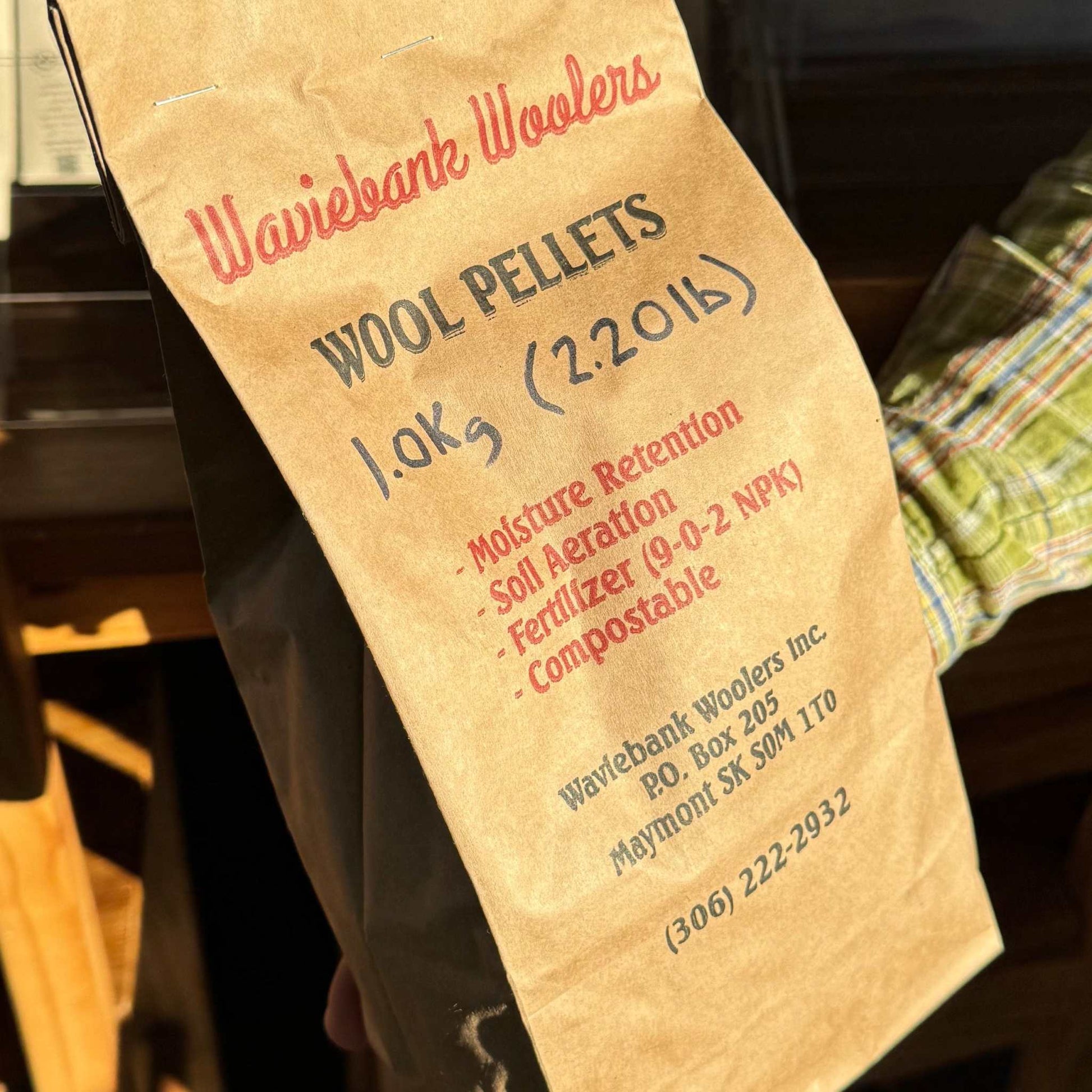 Hand holding a card labeled 'Wool Pellets' with text and a small image of pellets. Brown paper bag with text on a Wool Pellets by Waviebank Wollers - Regenerative Soil Amendment and Fertilizer available online only at MatchesSeeds.ca 