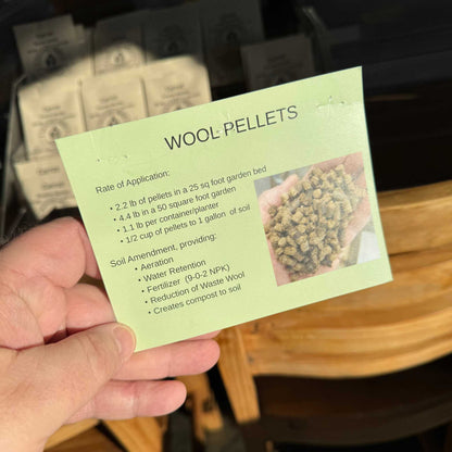 Hand holding a card labeled 'Wool Pellets' with text and a small image of pellets. Brown paper bag with text on a Wool Pellets by Waviebank Wollers - Regenerative Soil Amendment and Fertilizer available online only at MatchesSeeds.ca 