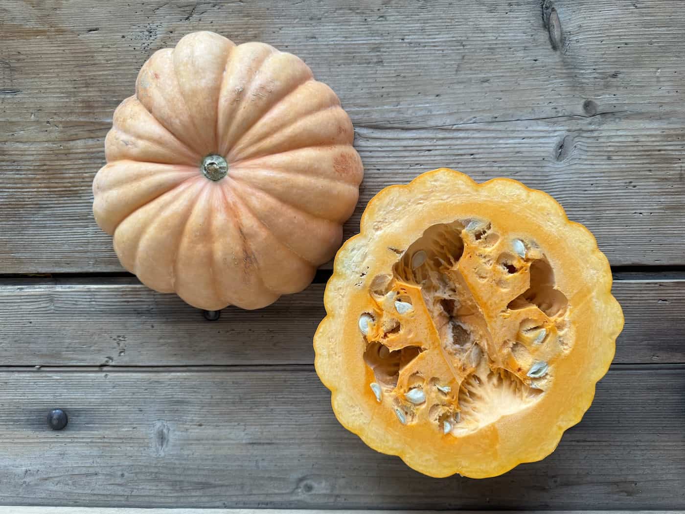 Moranga pumpkin with ribbed, pale salmon-colored rind next to a halved pumpkin showing seeds and bright orange flesh.